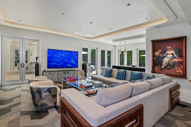 living room with a raised ceiling, carpet floors, and french doors