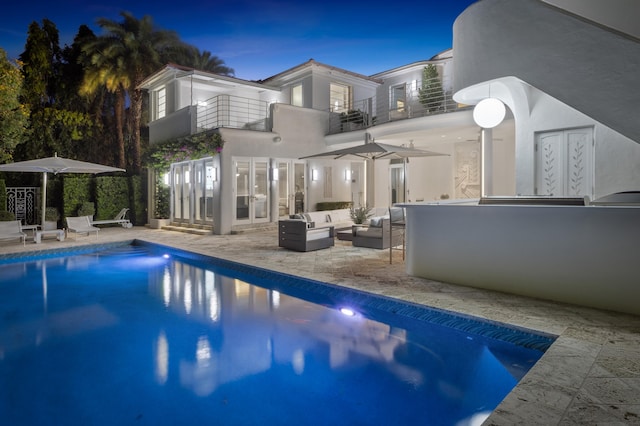 back house at dusk featuring outdoor lounge area, a balcony, and a patio area