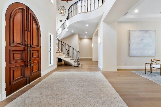 foyer entrance featuring ornamental molding, a chandelier, a high ceiling, and light wood-type flooring