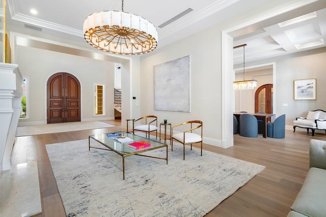 living room with coffered ceiling, a chandelier, ornamental molding, beamed ceiling, and hardwood / wood-style floors