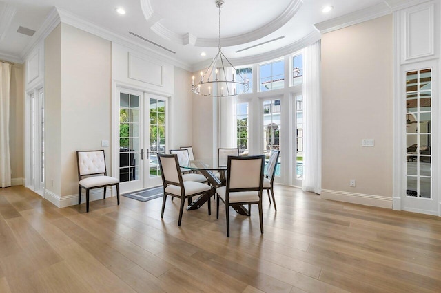 dining room featuring french doors, a tray ceiling, light wood-type flooring, and crown molding