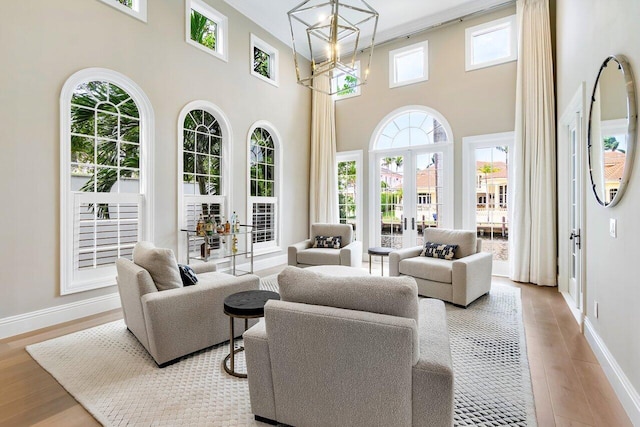 living room with a high ceiling, a healthy amount of sunlight, a notable chandelier, and light wood-type flooring