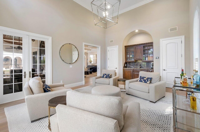 living room with ceiling fan, a high ceiling, wine cooler, ornamental molding, and light wood-type flooring