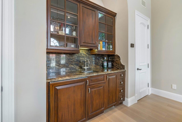 bar with tasteful backsplash, light hardwood / wood-style floors, sink, and dark stone countertops