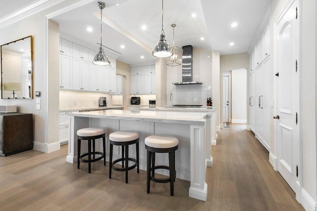 kitchen featuring a spacious island, white cabinetry, light stone counters, decorative light fixtures, and wall chimney range hood