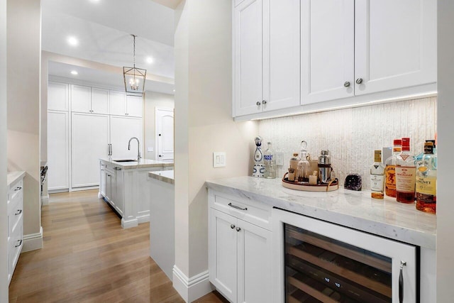 bar featuring sink, white cabinetry, hanging light fixtures, backsplash, and beverage cooler