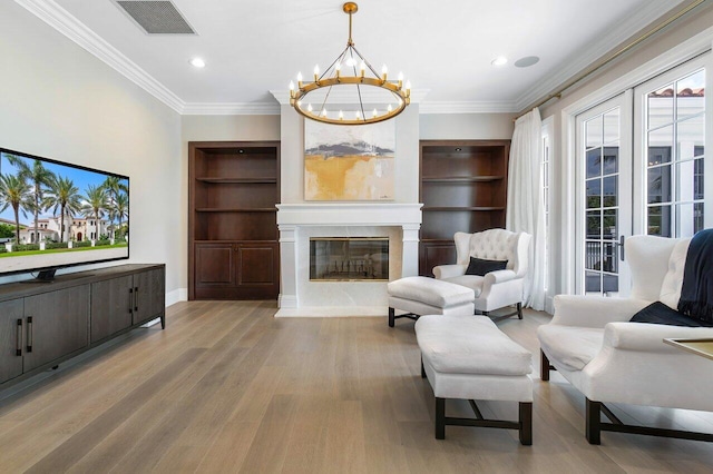 living room featuring crown molding, a chandelier, built in features, and light hardwood / wood-style floors