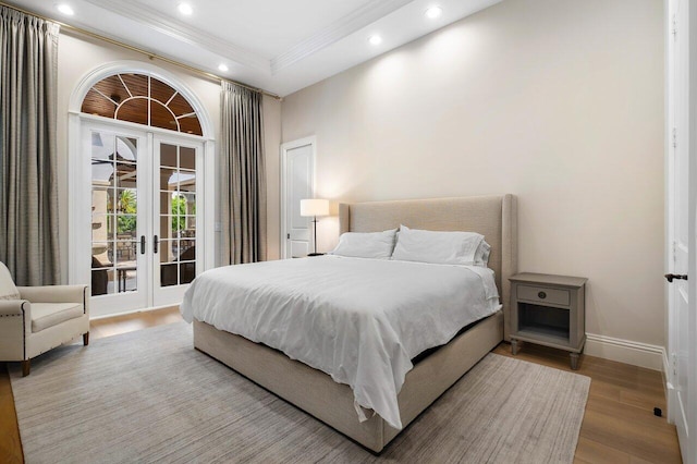 bedroom featuring a tray ceiling, light hardwood / wood-style flooring, french doors, and access to outside