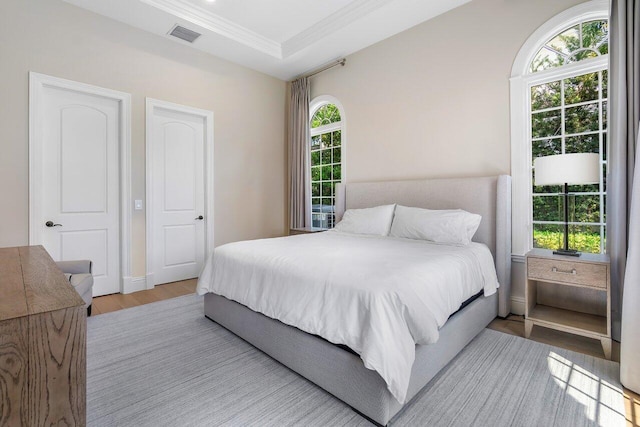 bedroom featuring multiple windows, a raised ceiling, crown molding, and light wood-type flooring