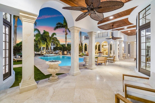 pool at dusk featuring ceiling fan and a patio area