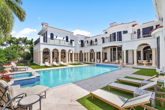 back of house with a swimming pool with hot tub, a patio, and a balcony