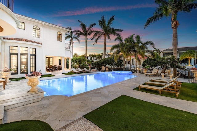 pool at dusk featuring french doors and a patio area