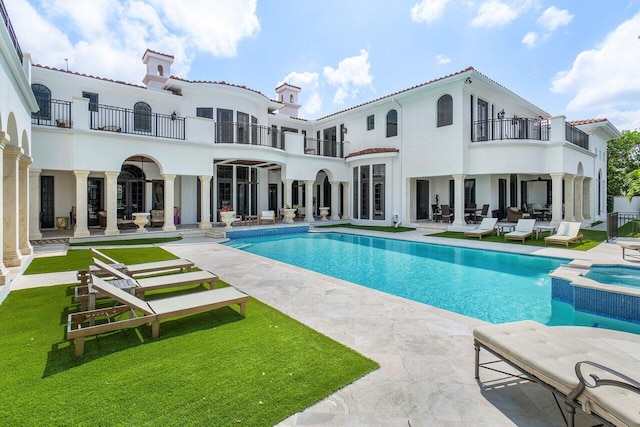 back of property featuring a balcony, a patio area, and a pool with hot tub