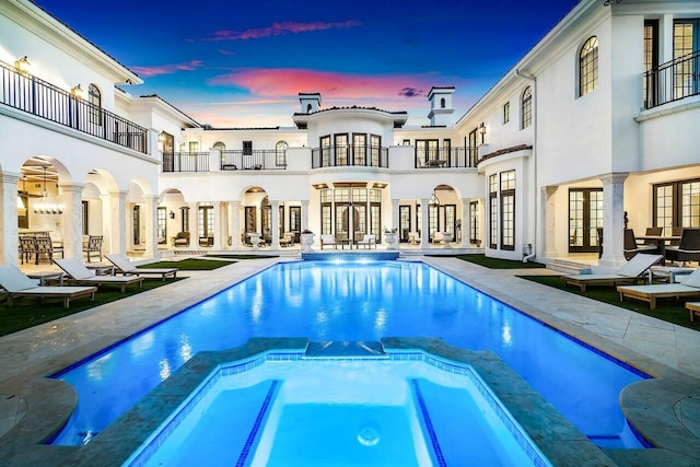 pool at dusk featuring an in ground hot tub, a patio area, and french doors