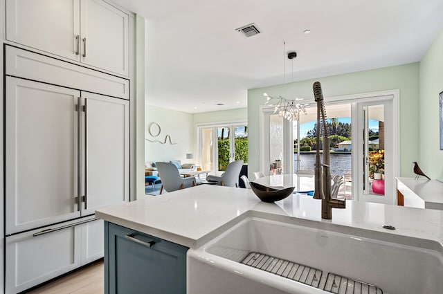 kitchen featuring paneled refrigerator, light stone counters, a notable chandelier, a water view, and decorative light fixtures