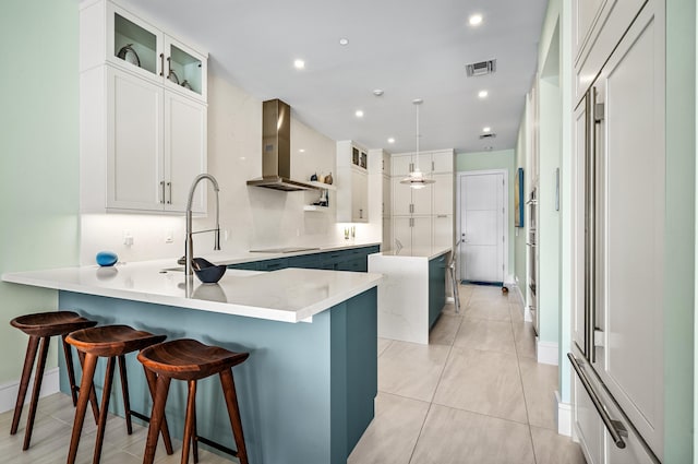 kitchen with white cabinets, a kitchen breakfast bar, kitchen peninsula, and wall chimney range hood