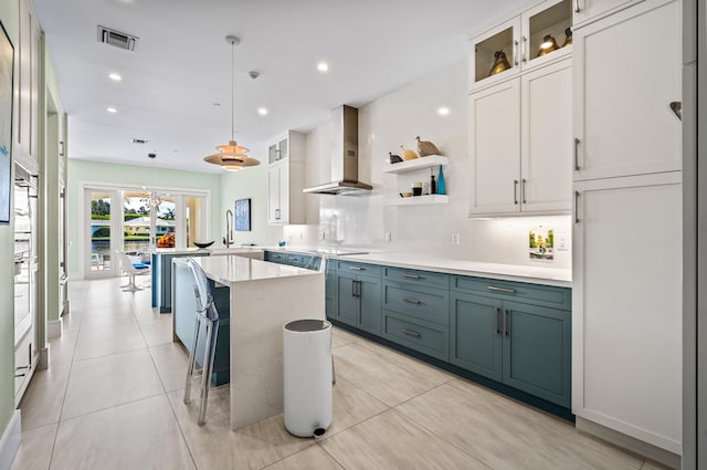 kitchen featuring white cabinets, sink, decorative light fixtures, wall chimney range hood, and a kitchen breakfast bar