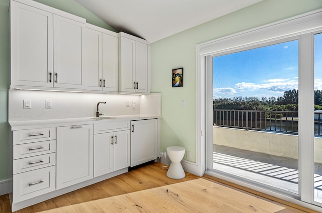 interior space with light wood-type flooring, sink, white cabinets, lofted ceiling, and a water view