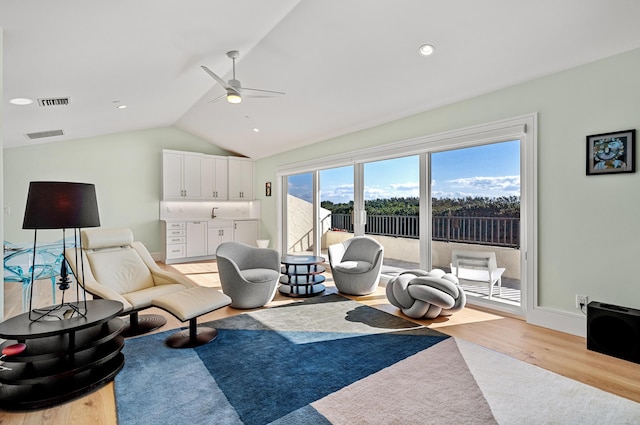 living room with ceiling fan, light hardwood / wood-style floors, and vaulted ceiling