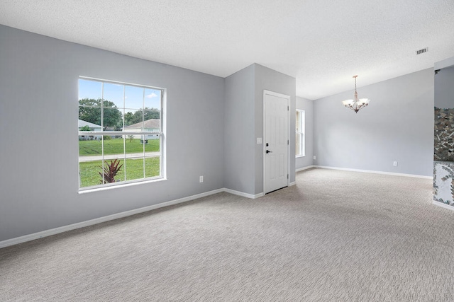 unfurnished room with a notable chandelier, a textured ceiling, and carpet flooring