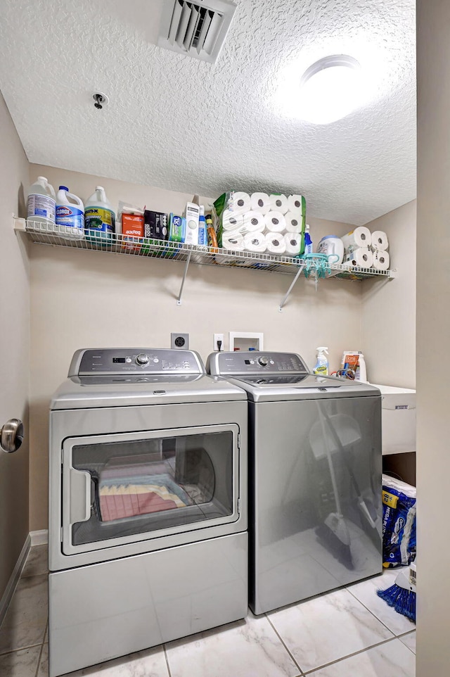 laundry room featuring washer and dryer, light tile patterned floors, and a textured ceiling