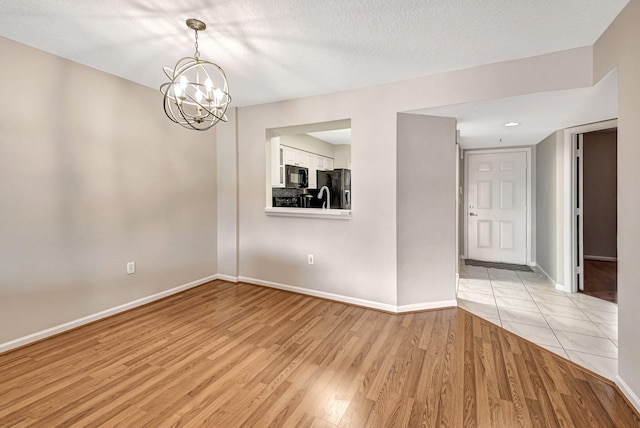 empty room with an inviting chandelier, light hardwood / wood-style flooring, and a textured ceiling