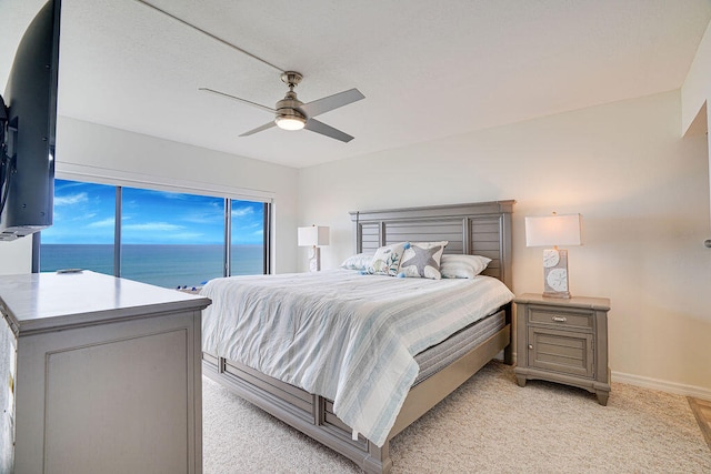 bedroom with a water view, ceiling fan, light colored carpet, and multiple windows