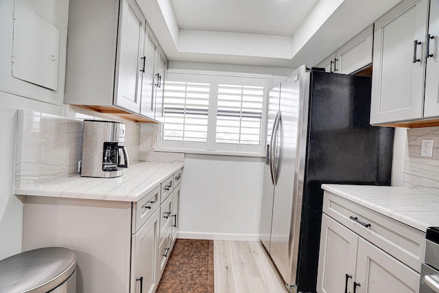 kitchen with a raised ceiling, light hardwood / wood-style flooring, stainless steel fridge with ice dispenser, white cabinetry, and decorative backsplash