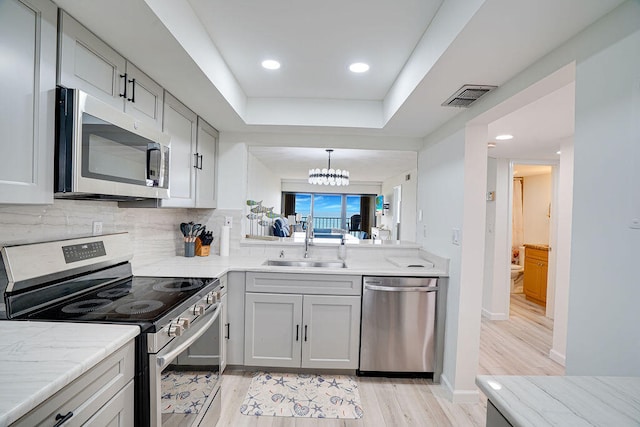 kitchen with a chandelier, tasteful backsplash, sink, light hardwood / wood-style flooring, and stainless steel appliances