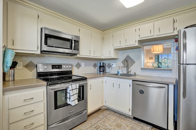 kitchen featuring sink, cream cabinetry, appliances with stainless steel finishes, tile countertops, and decorative backsplash