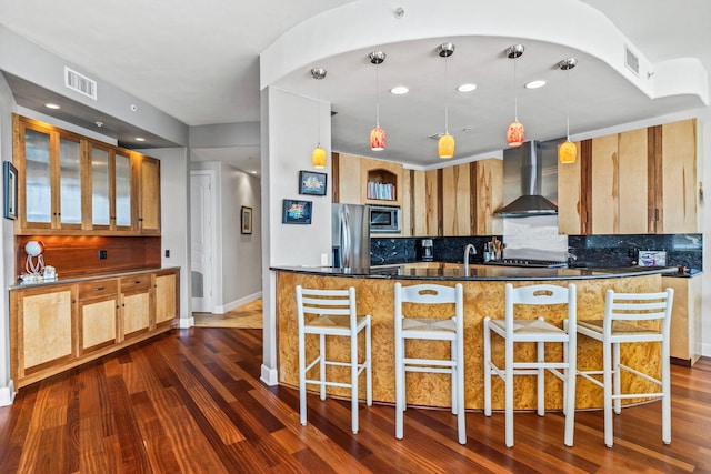 kitchen with dark wood-type flooring, wall chimney exhaust hood, hanging light fixtures, and stainless steel appliances