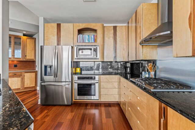 kitchen featuring dark stone counters, appliances with stainless steel finishes, dark hardwood / wood-style flooring, and wall chimney range hood