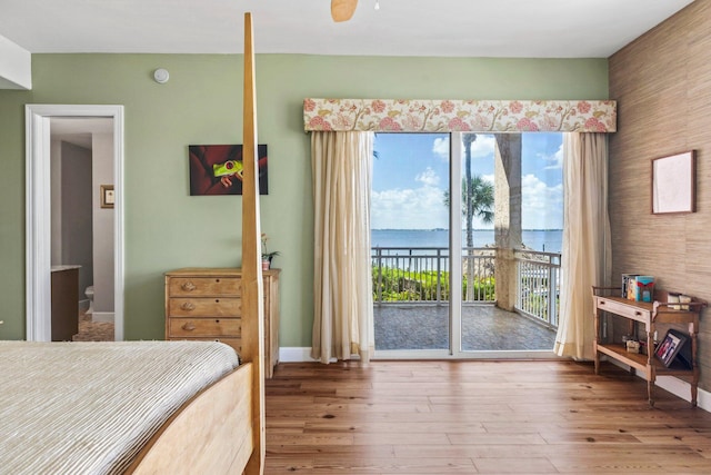 bedroom with ceiling fan, hardwood / wood-style flooring, ensuite bath, access to exterior, and a water view