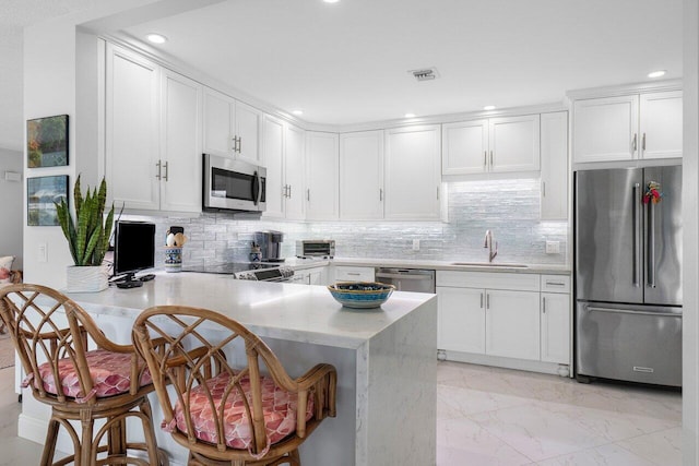 kitchen featuring marble finish floor, stainless steel appliances, white cabinetry, a sink, and a peninsula