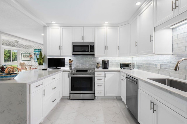 kitchen featuring white cabinets, appliances with stainless steel finishes, a peninsula, marble finish floor, and a sink