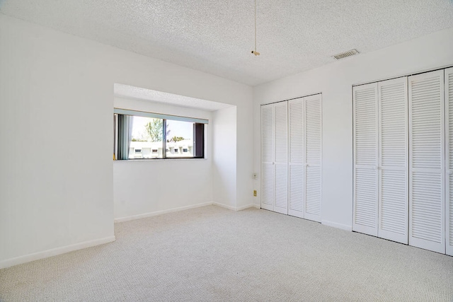 unfurnished bedroom with light carpet, two closets, and a textured ceiling