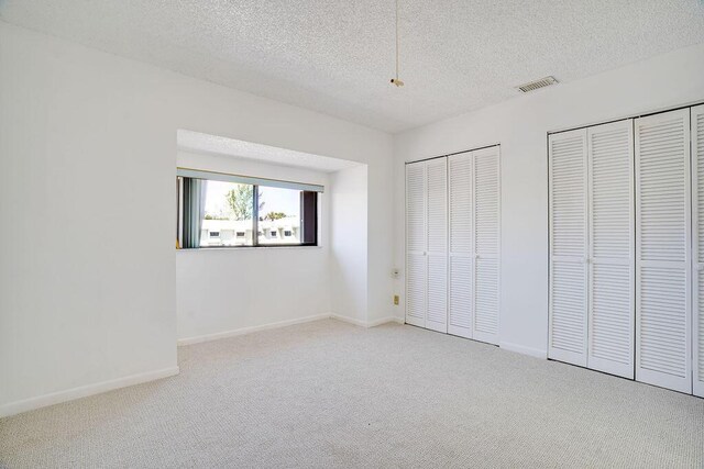 9427 S Ocean Dr Unit 60, Jensen Beach, FL 34957 - unfurnished bedroom with carpet flooring, a textured ceiling, visible vents, baseboards, and two closets