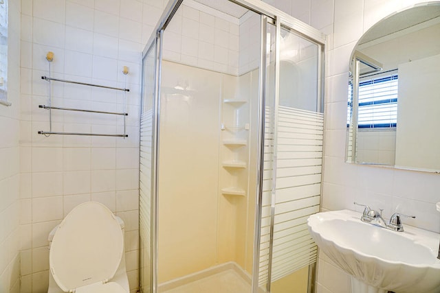 bathroom with tile walls, toilet, sink, and a shower with shower door