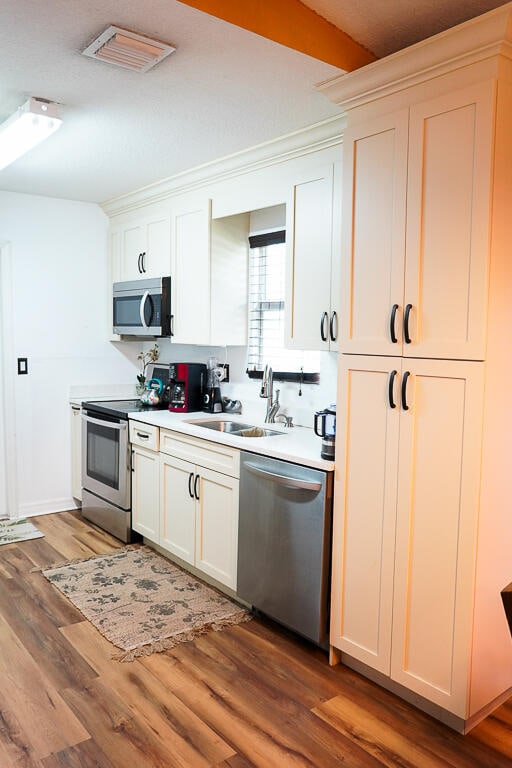 kitchen with stainless steel appliances, white cabinetry, wood-type flooring, and sink