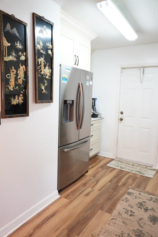 kitchen with stainless steel fridge, light hardwood / wood-style floors, and white cabinets