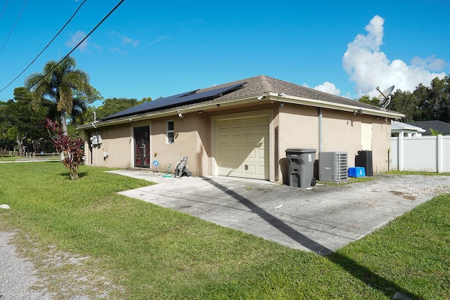 rear view of property featuring a lawn, a garage, solar panels, and central AC unit