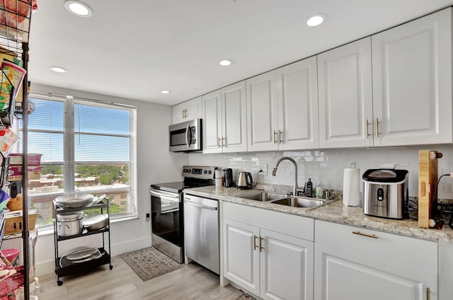 kitchen with sink, light wood-type flooring, a wealth of natural light, white cabinetry, and stainless steel appliances