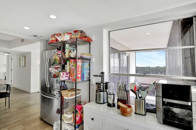 bar with stainless steel fridge, light hardwood / wood-style floors, and white cabinetry