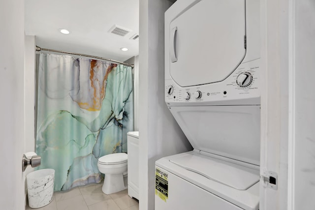 bathroom featuring stacked washer / drying machine and toilet