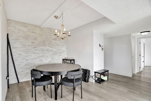 dining area with light hardwood / wood-style flooring, a textured ceiling, and a notable chandelier