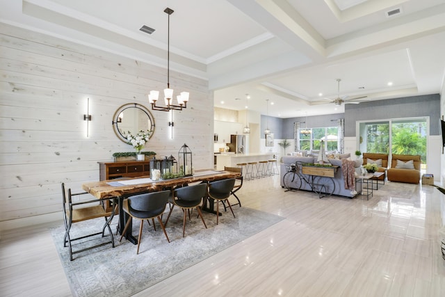 dining space with a tray ceiling, wooden walls, light tile patterned floors, and ceiling fan with notable chandelier