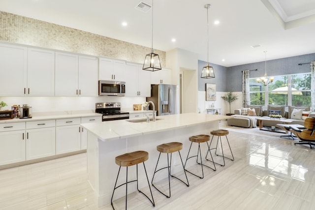 kitchen featuring stainless steel appliances, a kitchen island with sink, sink, decorative light fixtures, and white cabinetry