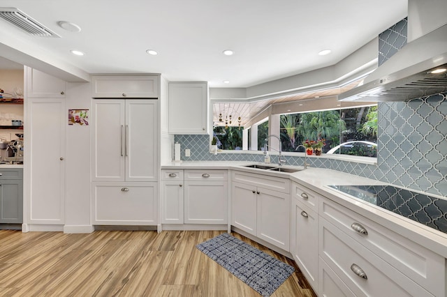 kitchen featuring decorative backsplash, light hardwood / wood-style flooring, wall chimney range hood, and sink