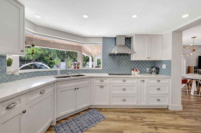 kitchen with white cabinets, wall chimney exhaust hood, light wood-type flooring, and sink