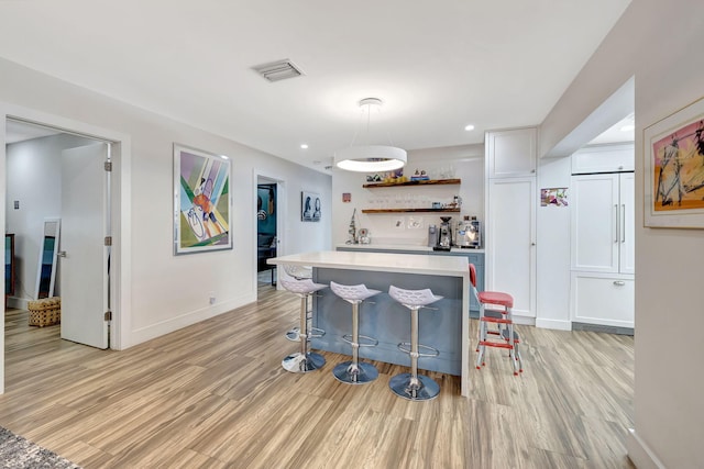 kitchen with light hardwood / wood-style flooring, white cabinetry, decorative light fixtures, and a breakfast bar area